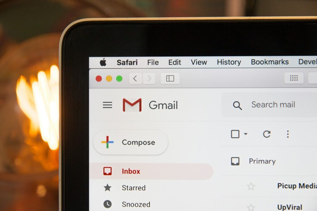 Een close-up van een laptopscherm met de Gmail-interface. De knop Opstellen is zichtbaar, samen met de mappen Inbox, Starred en Snoozed. De webpagina is geopend in de Safari-browser, met een fel licht dat wazig is op de achtergrond.