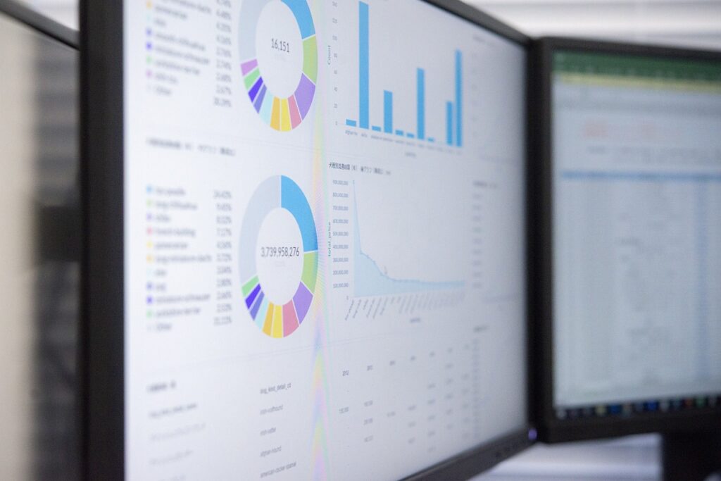 Computermonitoren die datavisualisaties weergeven, waaronder cirkeldiagrammen, staafdiagrammen en lijndiagrammen, op een spreadsheet. De schermen tonen statistische informatie en verschillende gekleurde secties die verschillende datacategorieën vertegenwoordigen.