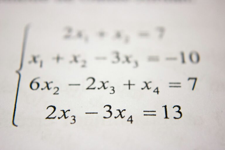 Close-up van een pagina met een stelsel lineaire vergelijkingen. De vergelijkingen zijn: x₁ + x₂ - 3x₃ = -10, 6x₂ - 2x₃ + x₄ = 7, en 2x₃ - 3x₄ = 13, allemaal ingesloten in een linker accolade.