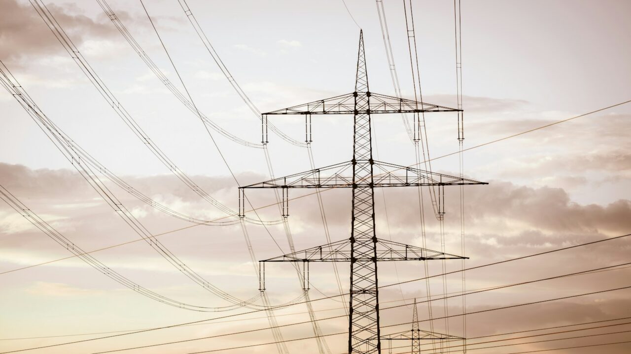 Hoogspanningsleidingen op hoge metalen torens strekken zich uit over de horizon tegen een bewolkte hemel en illustreren de energie-infrastructuur.