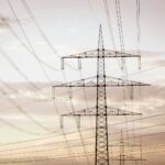 Hoogspanningsleidingen op hoge metalen torens strekken zich uit over de horizon tegen een bewolkte hemel en illustreren de energie-infrastructuur.