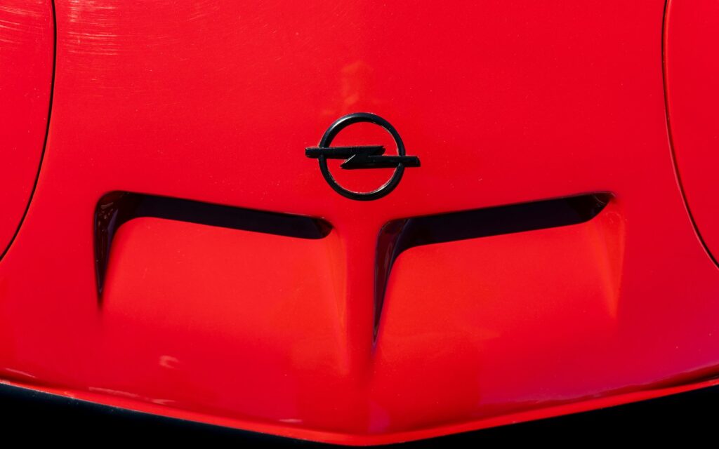 Close-up van een rode motorkap met het Opel-logo. De motorkap heeft twee prominente luchtroosters.