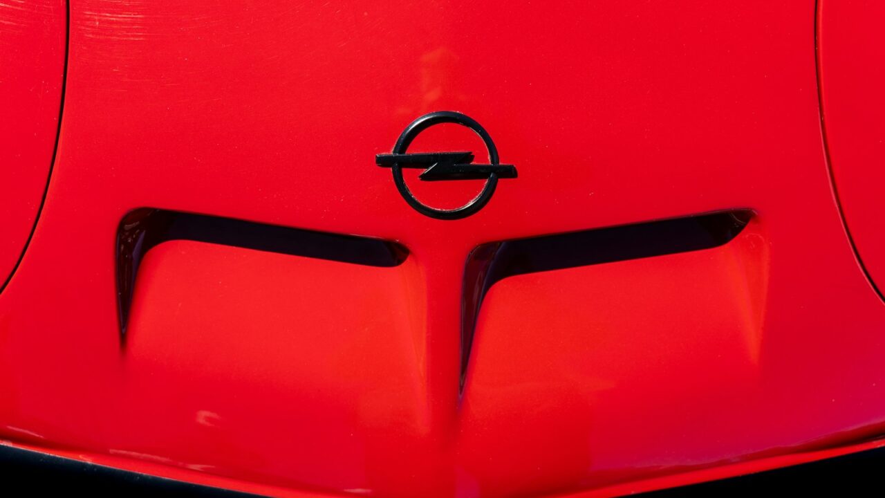 Close-up van een rode motorkap met het Opel-logo. De motorkap heeft twee prominente luchtroosters.