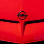 Close-up van een rode motorkap met het Opel-logo. De motorkap heeft twee prominente luchtroosters.