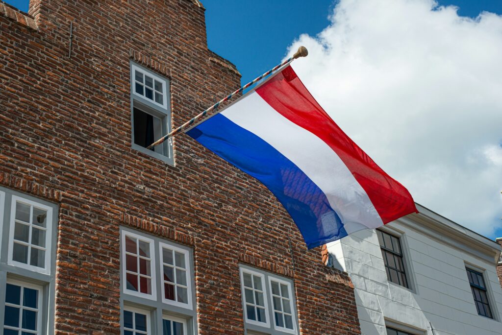 Een Nederlandse vlag wappert buiten een bakstenen gebouw tegen een gedeeltelijk bewolkte lucht.