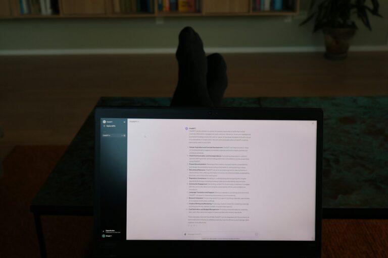 Een persoon zit in een donkere kamer met zijn voeten op een tafel en kijkt naar een laptopscherm met tekst. Op de achtergrond staan een boekenplank en een potplant.