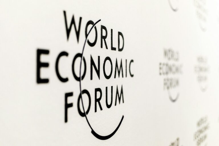 Zwarte tekst op een witte achtergrond luidt "World Economic Forum" met een cirkelvormige lijn die de letters kruist. De tekst wordt herhaald op de achtergrond.