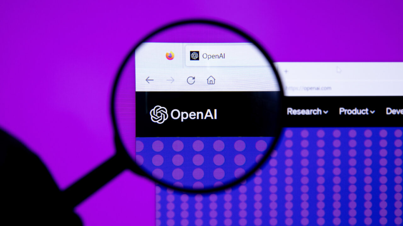 Een vergrootglas richt zich op het OpenAI-logo en de websiteheader op een computerscherm, terwijl een paarse achtergrond zichtbaar is achter de monitor.