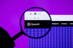 Een vergrootglas richt zich op het OpenAI-logo en de websiteheader op een computerscherm, terwijl een paarse achtergrond zichtbaar is achter de monitor.