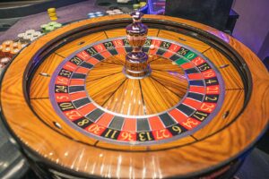 Een close-up van een roulettewiel met rode, zwarte en groene genummerde vakjes, een zilveren bal op het draaiende wiel en stapels casinofiches zichtbaar op de achtergrond.